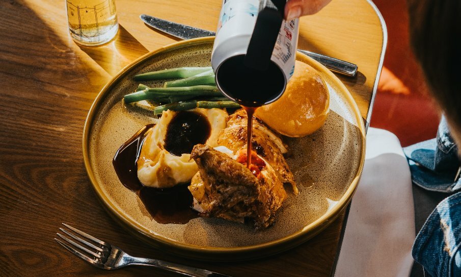 Roast chicken dinner with three sides on a brown table with gravy being poured onto the plate.