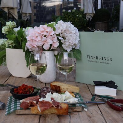 Grazing board and glasses of wine next to vases of flowers and shopping bags.