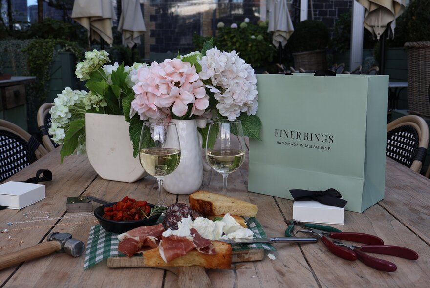 Grazing board and glasses of wine next to vases of flowers and shopping bags.