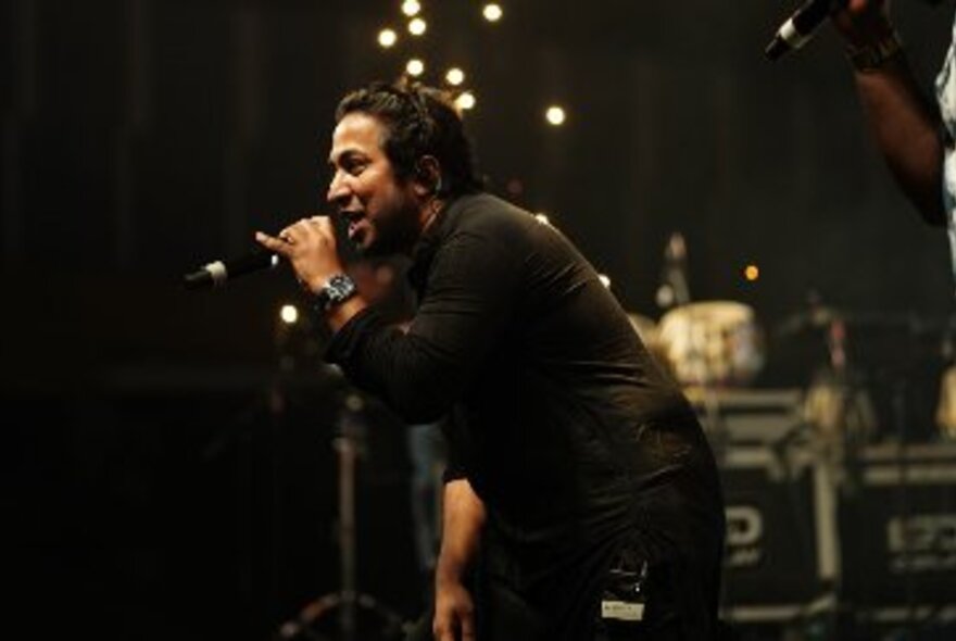 Actor and musician Vineeth Sreenivasan, a man aged about 40 years, singing into a microphone the holds in his hand, in profile view.