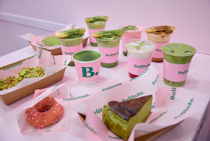 A selection of matcha drinks and desserts in pink takeaway packaging.