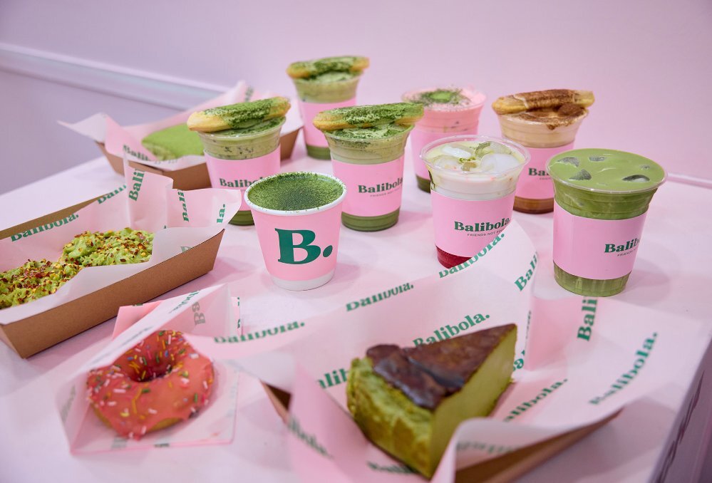 A selection of matcha drinks and desserts in pink takeaway packaging.