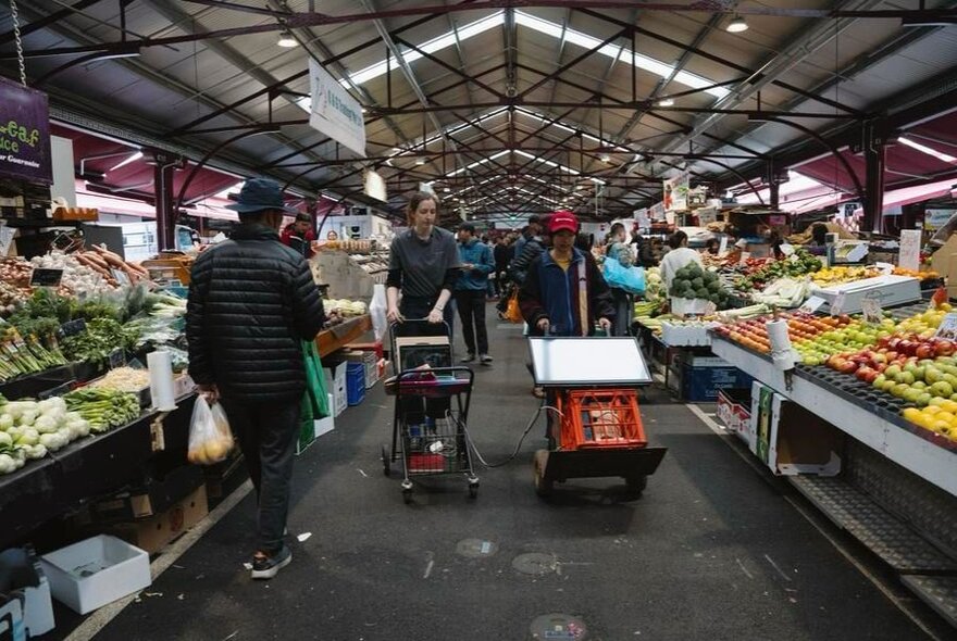 Vic Market scene with traders and customers in fruit section stalls.