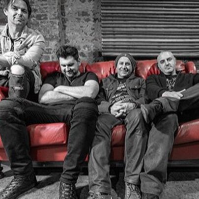 Four men slouching on a red couch.