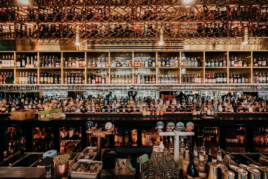 A view of the bar at Left Bank showing many rows of bottles behind the bar service area, gold trim and spotlights.