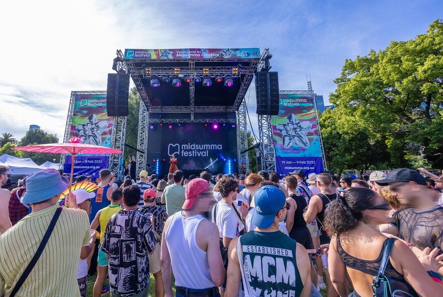Festival crowds watching a stage on a sunny day.