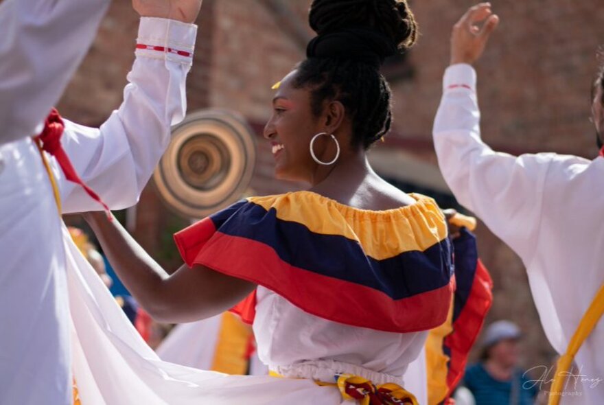 A traditional Spanish dancer wearing a white dress with a red, blue and yellow striped shoulder ruffle.