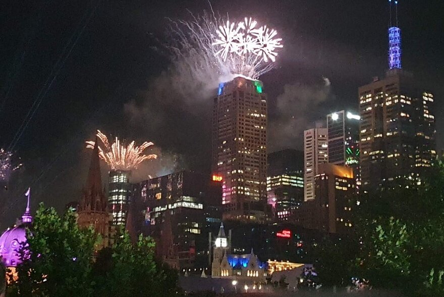 View of fireworks exploding in the night sky over Melbourne city buildings. 