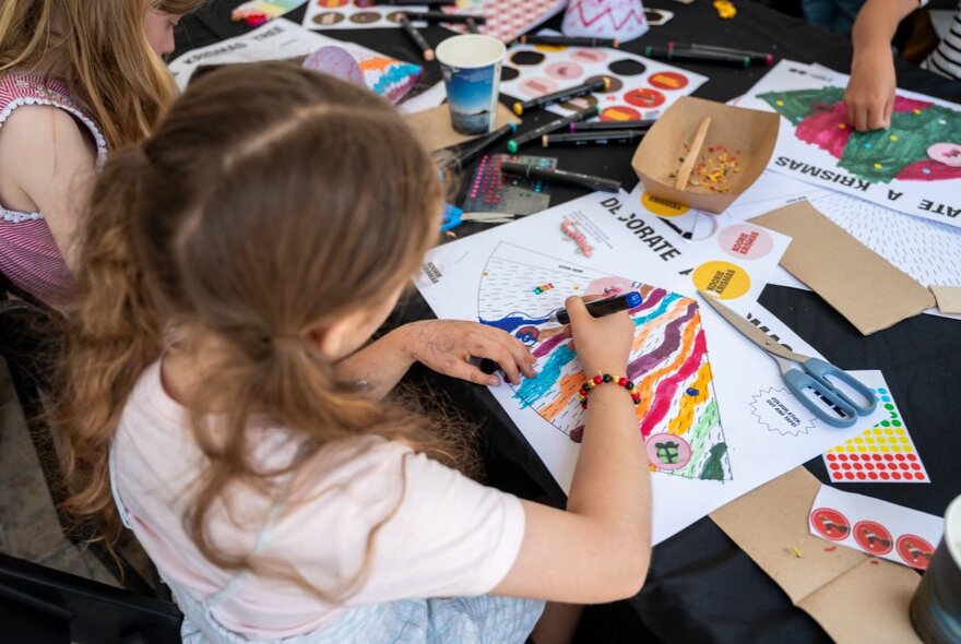 Looking over the shoulder of a small girl with pigtails colouring in. 