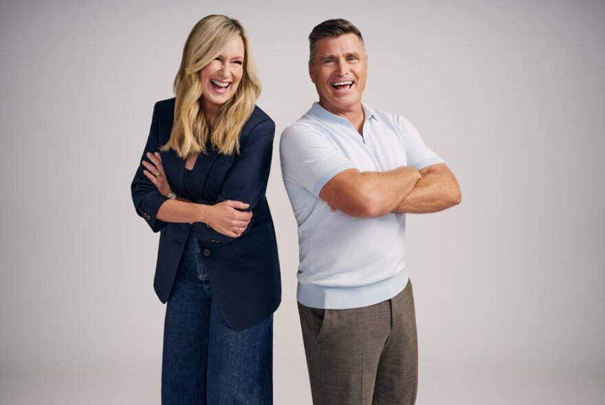 TV presenters Melissa Doyle and Shane Crawford standing back to back and laughing, both with their arms crossed over their chests.