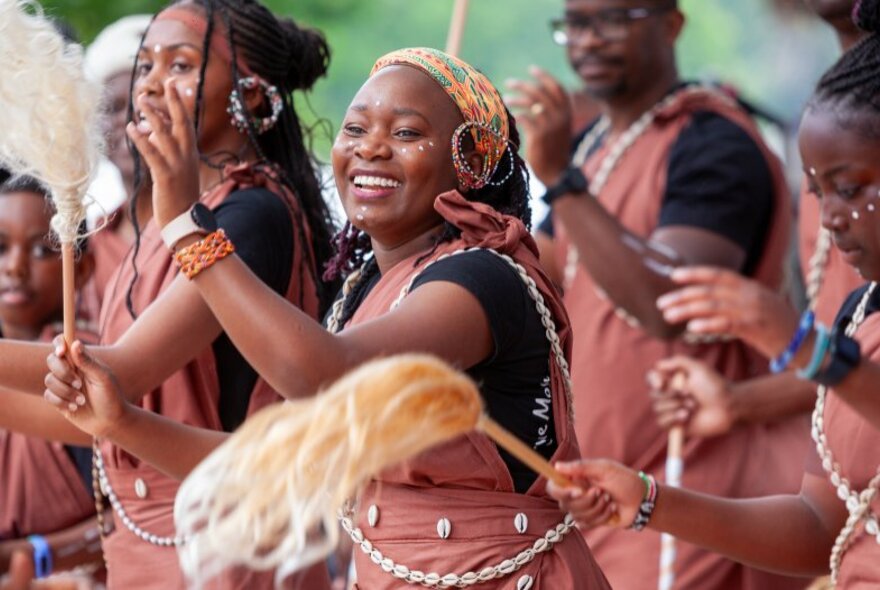 African dancers performing at a festival, the central woman smiling warmly. 