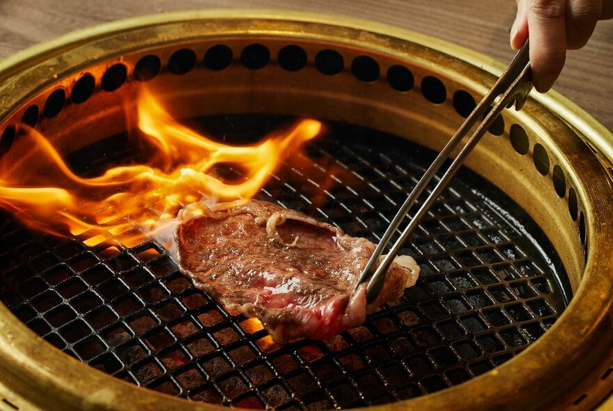 Wagyu beef held with chopsticks over a grill.