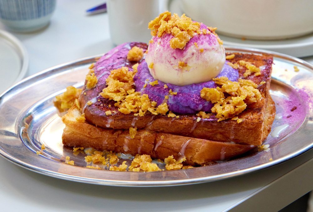 Thick piece of brioche toast on a silver plate topped with ube, ice cream and cornflakes.