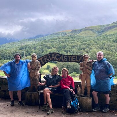 A group of walkers resting in Triacastela, Spain, during their journey on the Camino de Santiago, with green hills in the background.