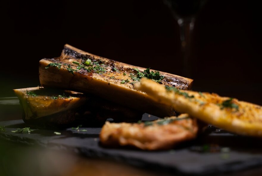 A side shot of roasted bone marrow on a black plate.