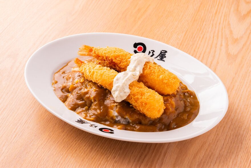 Japanese curry with crumbed prawns on top in a white bowl on a wooden surface.