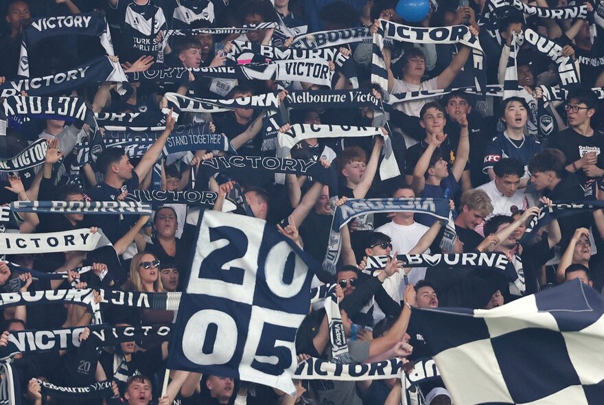 A crowd of Melbourne Victory A-League supporters all holding up scarves or flags.