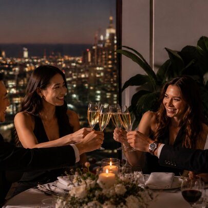 A group of people toasting with champagne at a dining table with a view of Melbourne at night in the background. 