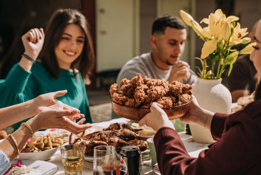 People sharing a platter of chicken at an outdoor table.