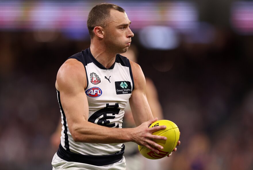 A Carlton AFL football player holding the ball during a match.