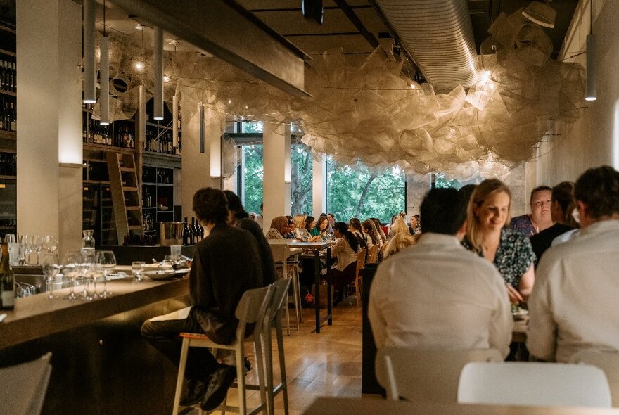 Restaurant interior with people seated at tables along a wall and at the bar.