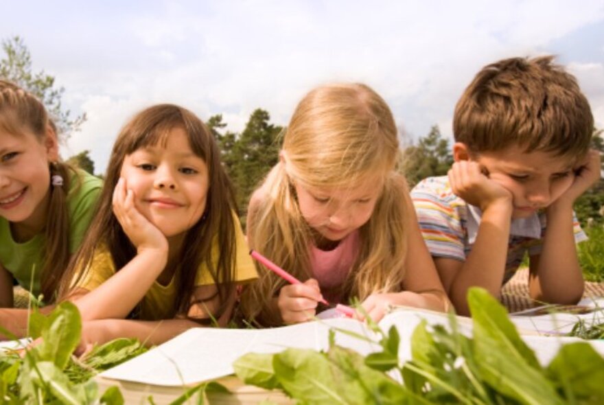 Children lying on grass with books and pencils.