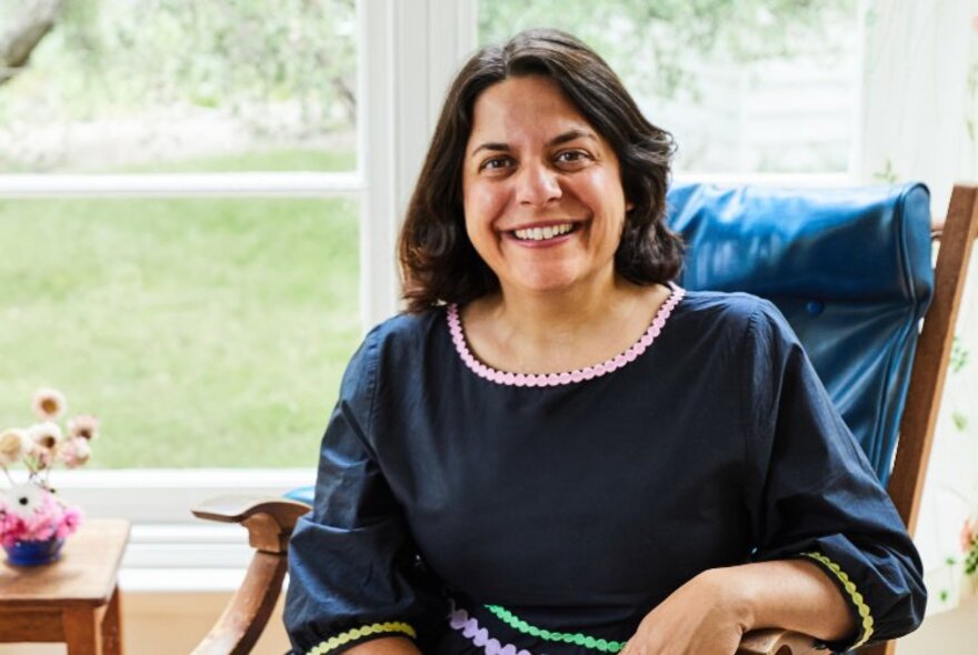 Author, Jaclyn Crupi, pictured sitting in an Eames armchair in front of a window, smiling.