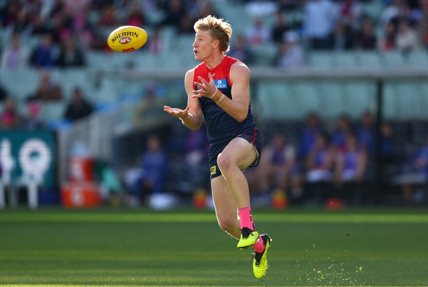 A Melbourne AFL football player running and about to catch the ball during a match.