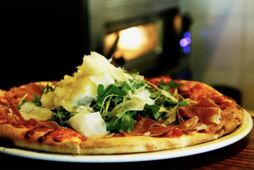 Close up of a pizza with prosciutto, rocket and shaved parmesan.