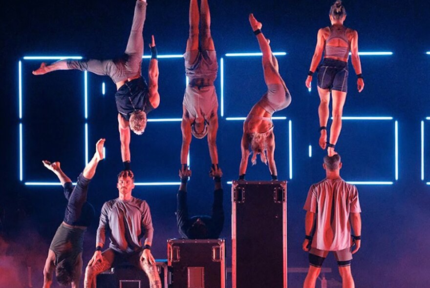 A group of performance acrobats in front of a stage background with illuminated lettering. 