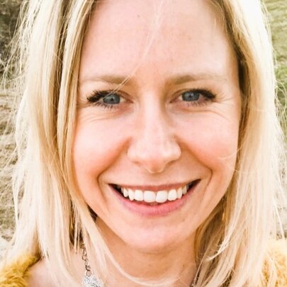 Close up of a woman with blonde hair smiling in a park. 
