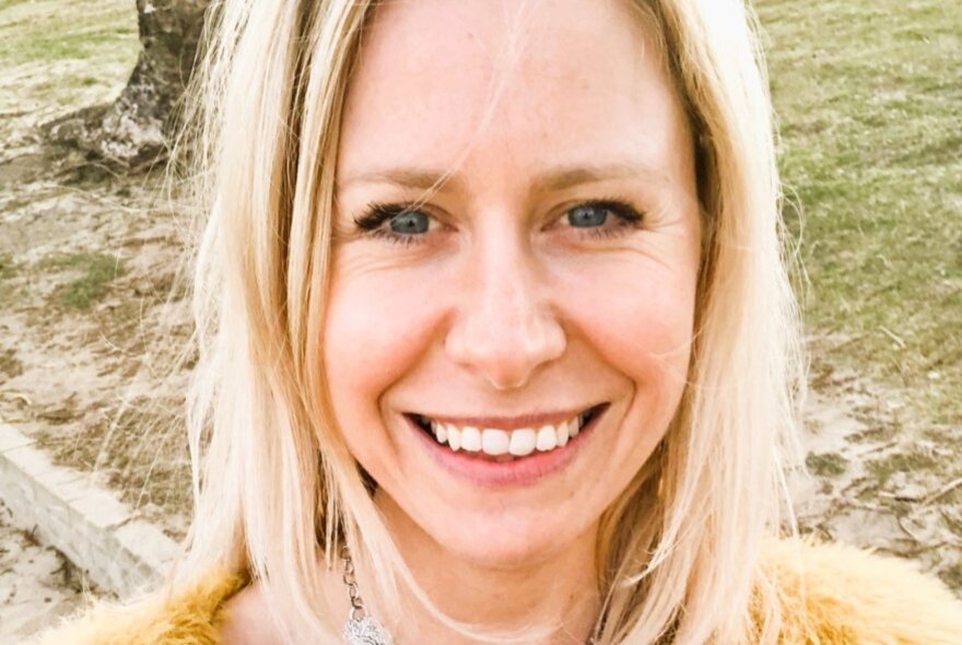 Close up of a woman with blonde hair smiling in a park. 