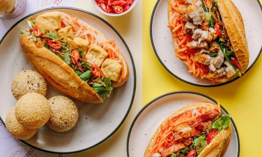 Birdseye view of three plates of banh mi. One of the plates has four round sesame donuts on it.