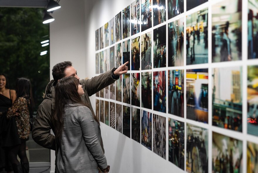 People looking and pointing at photographic artworks on a wall in a gallery.