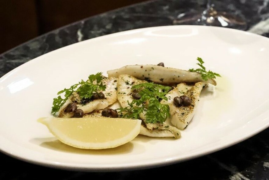 Pasta dish on a white plate with parsley and lemon.