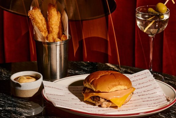 A cheeseburger, fries standing up in a steel beaker and a martini.