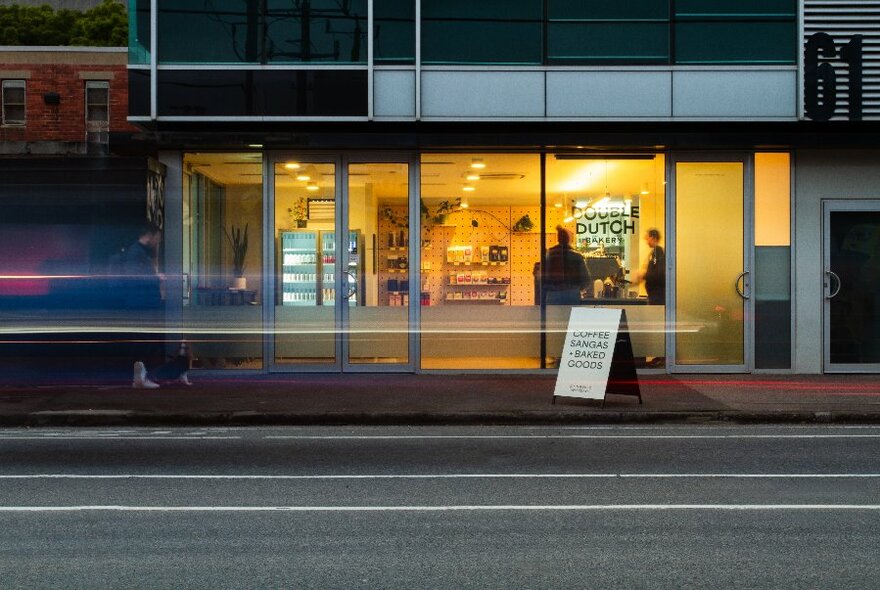 Illuminated bakery storefront at dusk with light movement from a passing car.