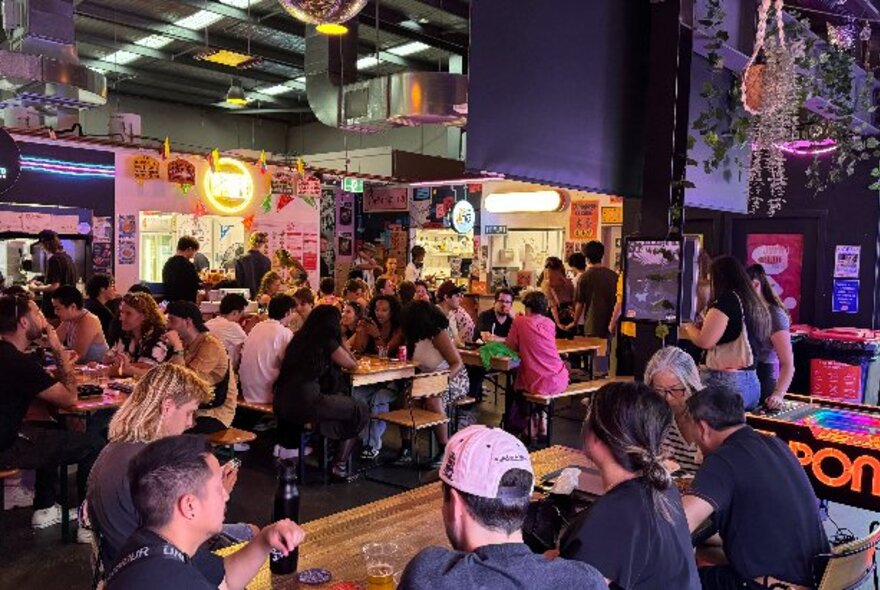 People seated at outdoor dining tables at a festival at EziStreat with food stalls in the background.