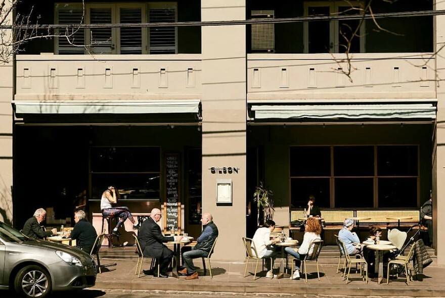 Gilson exterior with outdoor tables and 1st-floor apartment balconies.