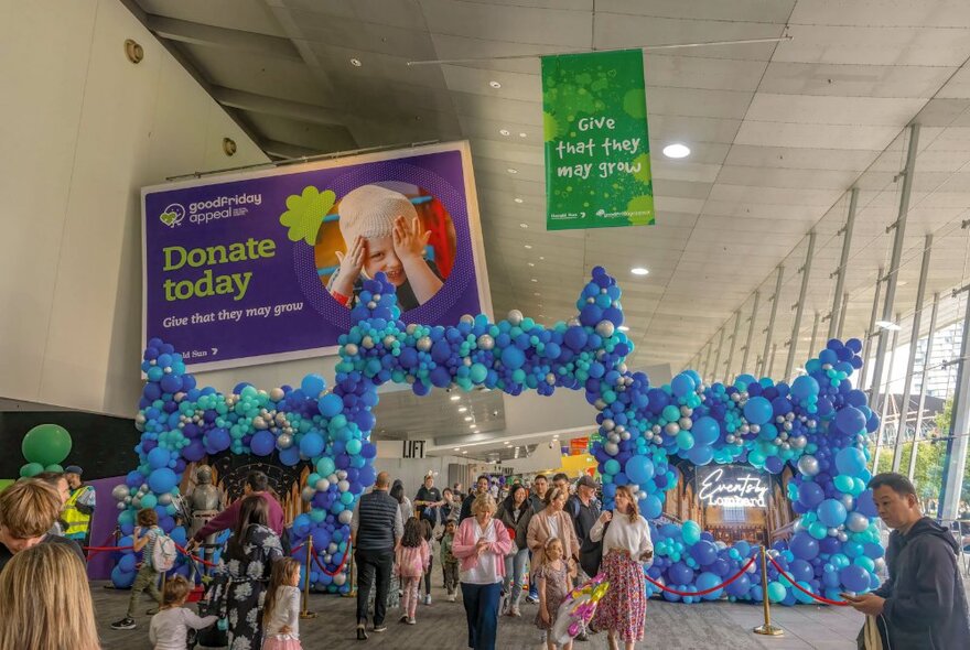 Families in a large venue, walking through an entry formed by balloons with banners overhead.