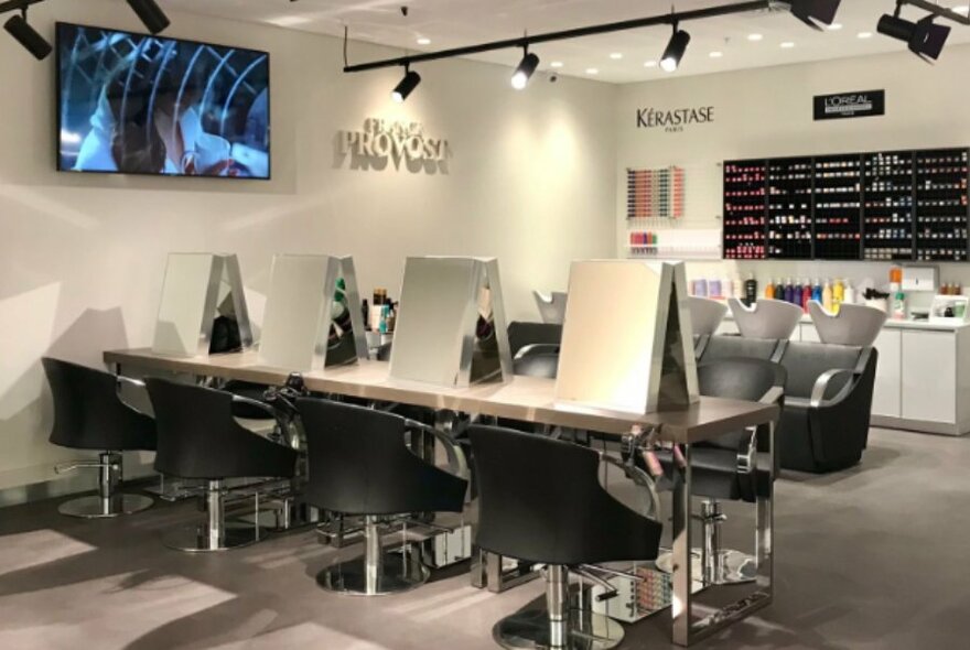 Salon interior with work tables and seating, overhead lighting and screen.