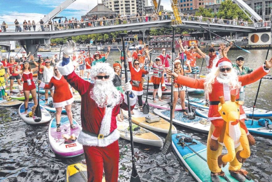 People dressed in Santa costumes on SUP boards on the Yarra River.