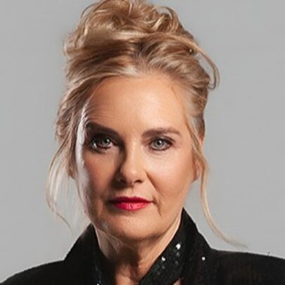 Woman with blonde hair piled on top of her head in a bun, wearing red lipstick and eye makeup.
