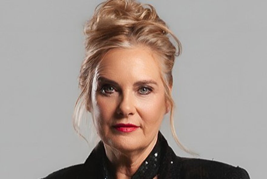 Woman with blonde hair piled on top of her head in a bun, wearing red lipstick and eye makeup.