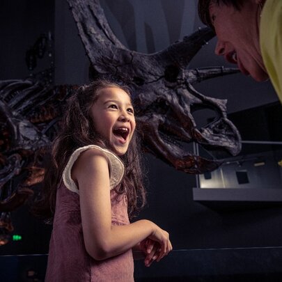 Child looking over right shoulder with delighted smile, dark dinosaur model behind.