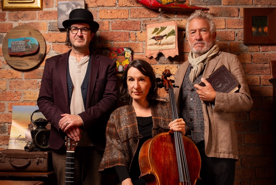 Two musicians and a man with a book standing next to a brick wall.