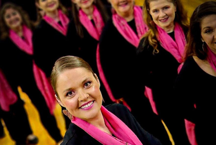 Choir members wearing dark jackets and vibrant pink scarves posing for a group photo.