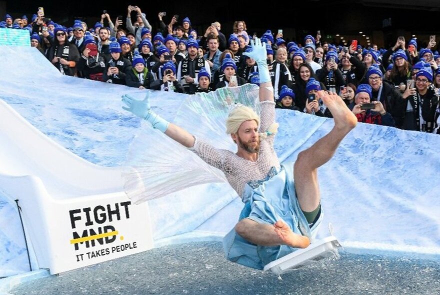 Hamish Blake dressed as Elsa going down a slide into an ice pool.