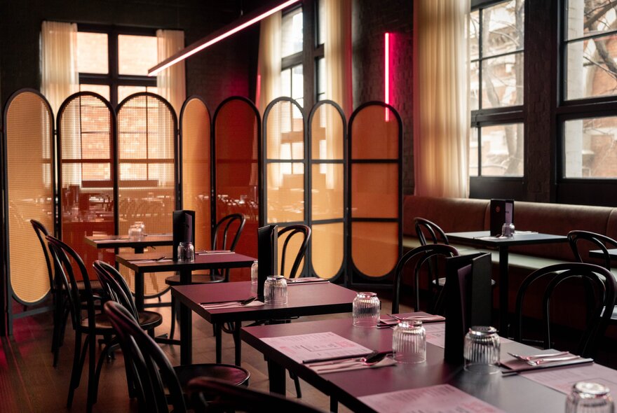 An empty restaurant space with tall windows, and a traditional Chinese screen dividing the room. 