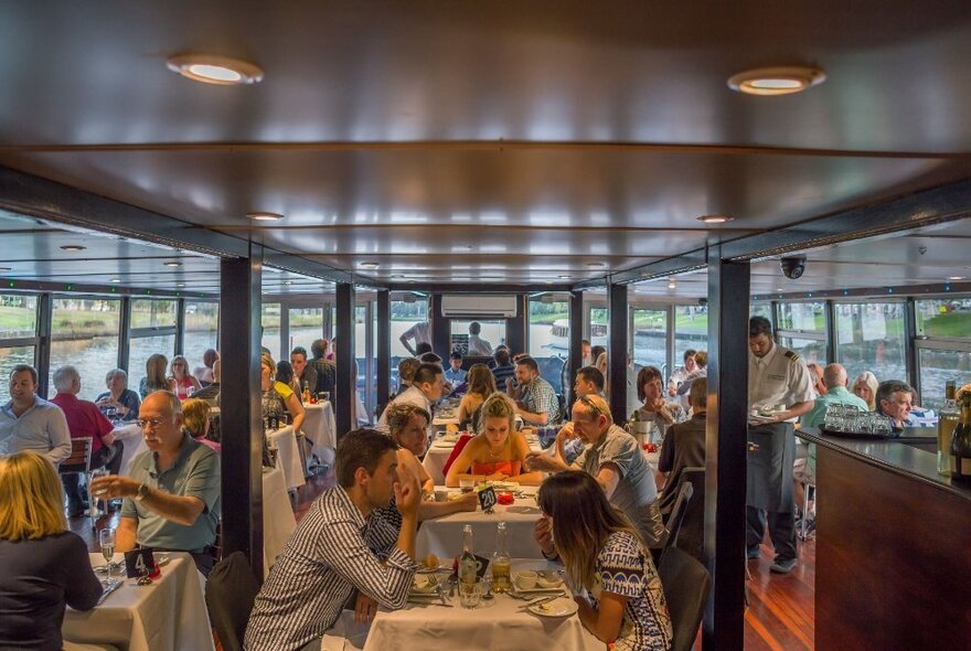 The interior of a floating river cruise restaurant with patrons eating lunch.